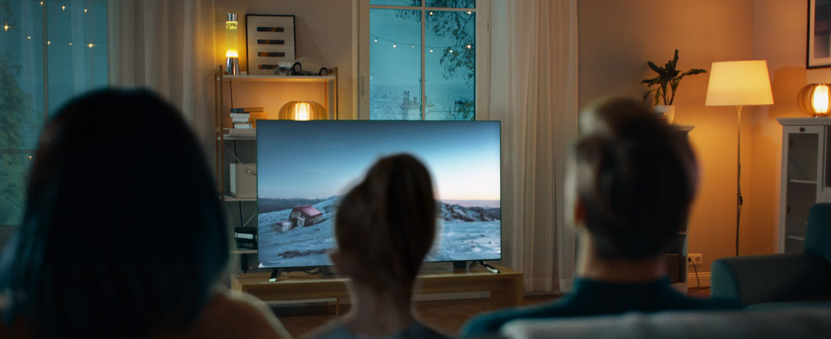Une famille rassembl&eacute;e dans un salon, regardant un grand t&eacute;l&eacute;viseur &agrave; &eacute;cran plat