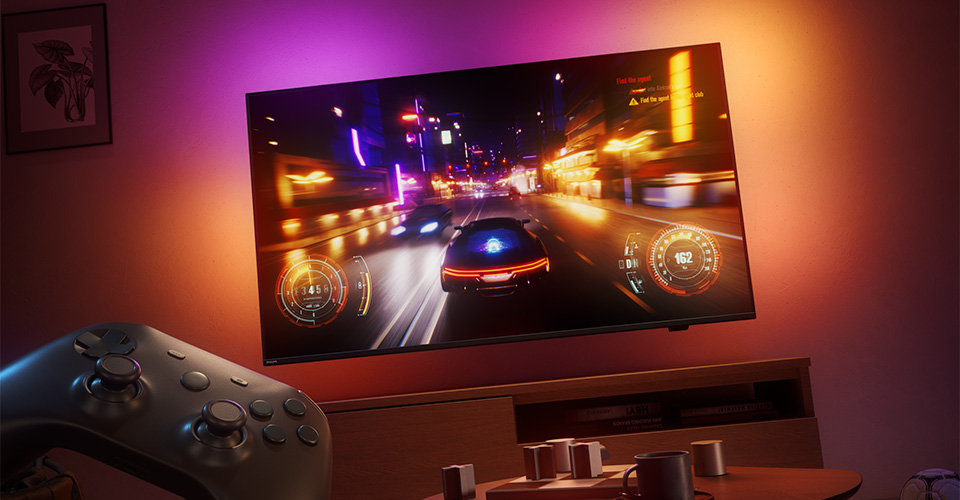 Un jeu vid&eacute;o de course est affich&eacute; sur un t&eacute;l&eacute;viseur Philips Ambilight dans une pi&egrave;ce faiblement &eacute;clair&eacute;e
